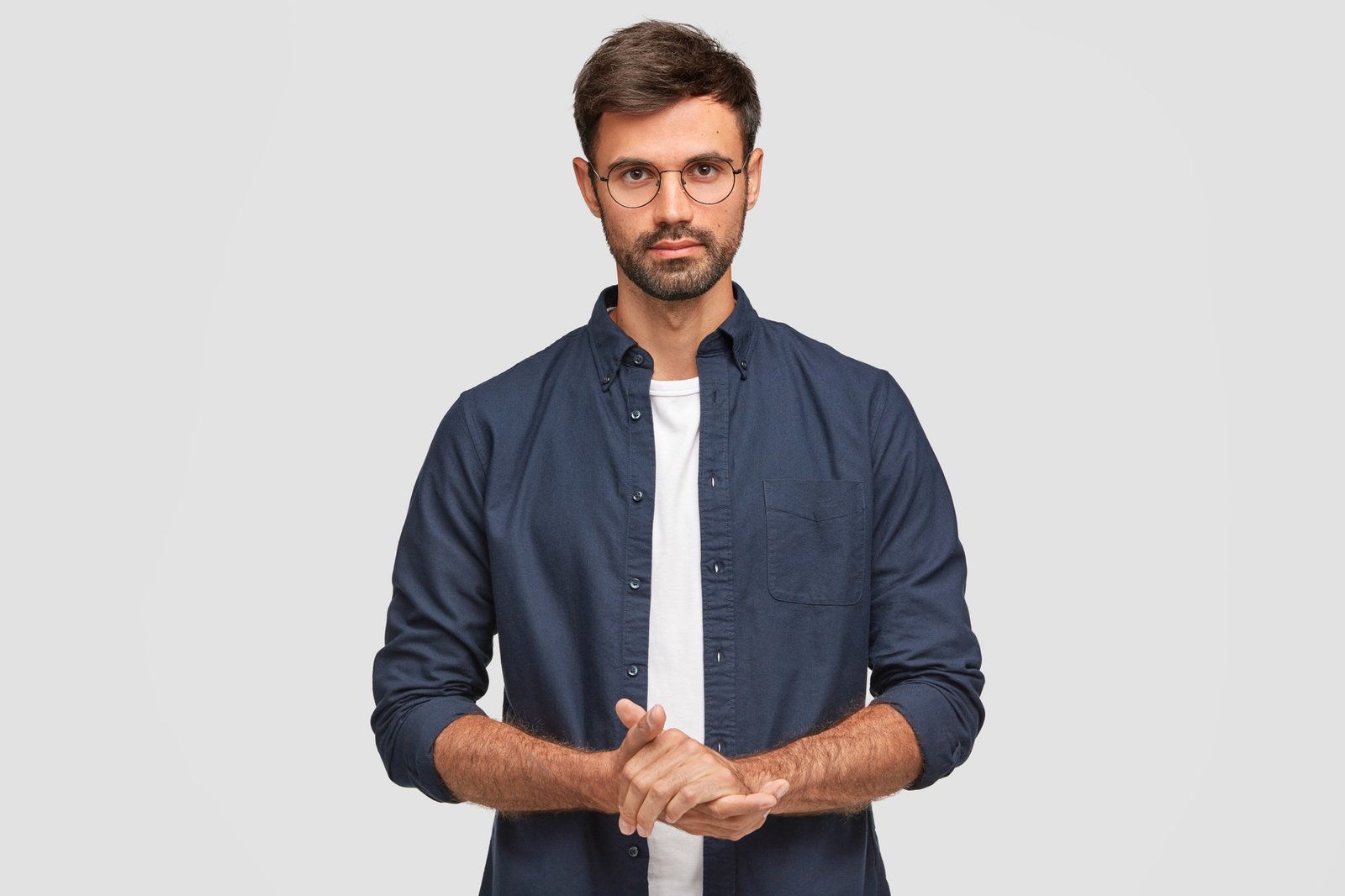 Waist Up Portrait Handsome Serious Unshaven Male Keeps Hands Together Dressed Dark Blue Shirt Has Talk With Interlocutor Stands Against White Wall Self Confident Man Freelancer